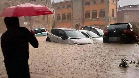 Uomo con ombrello che guada macchine immerse nel fango